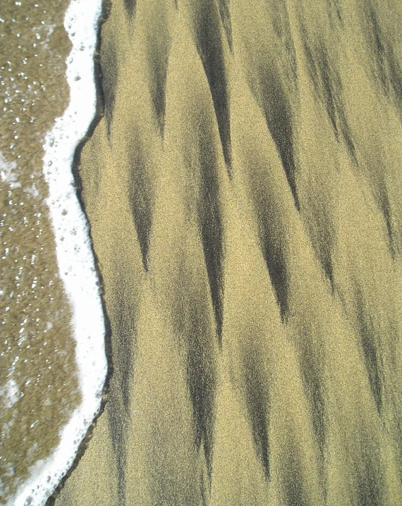 the beach sand is black and has waves lapping up around it