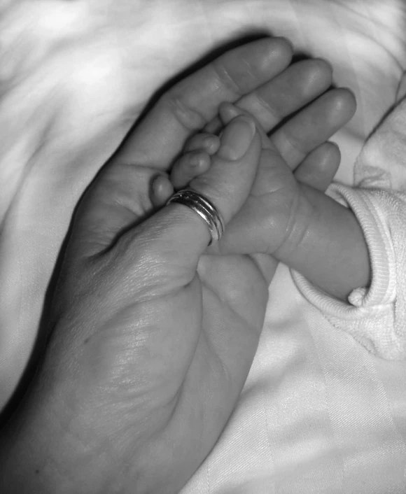 black and white pograph of a baby holding the hand of its mother