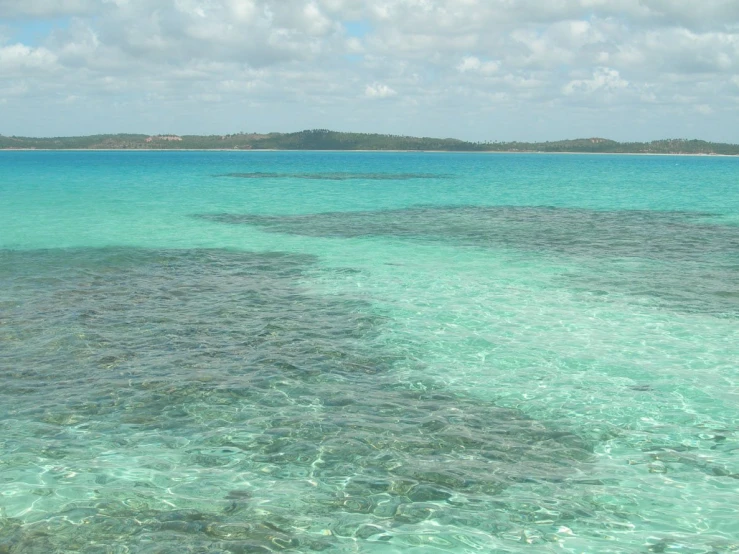 a calm blue ocean with the sky above and an island in the distance