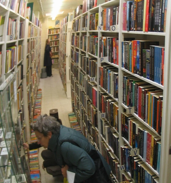 a person crouching down near a bookshelf filled with books