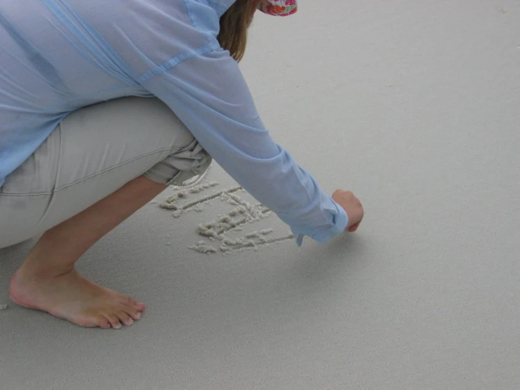 a girl in a blue shirt is putting her hand prints in the sand