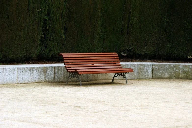 a wooden park bench sits in front of a concrete wall