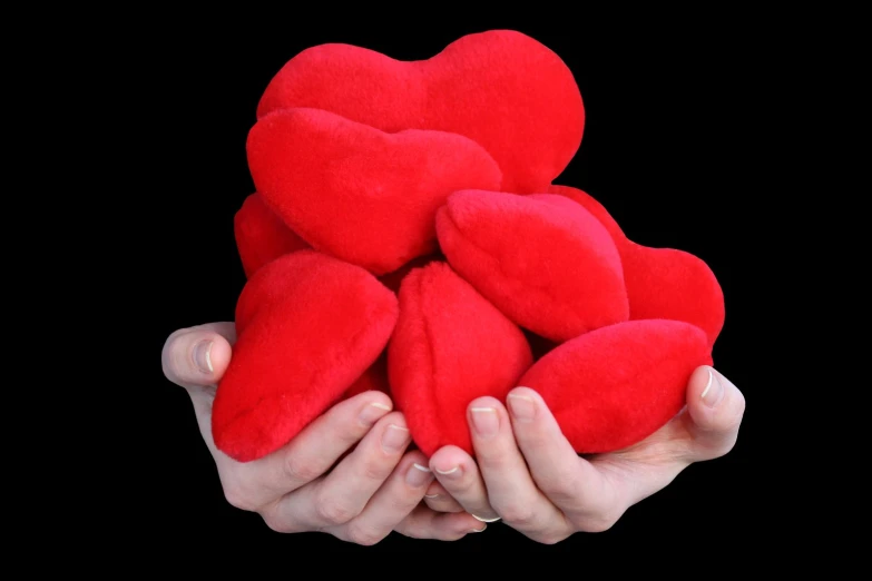 two hands holding a heart shaped red plush object