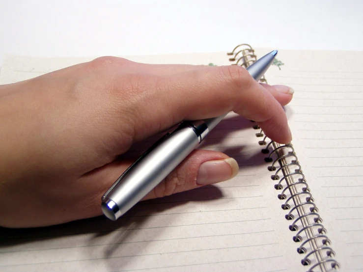 woman's hand holding pen and writing on lined notebook