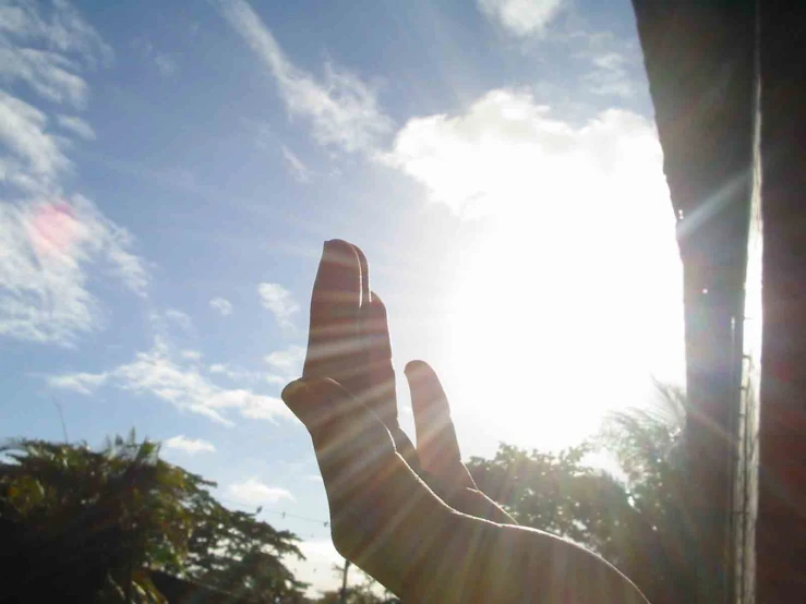 someone's hand reaching upward into the sky with the sun shining through it