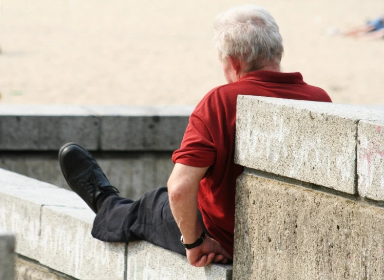 a man with his legs crossed sitting against the side of a cement wall