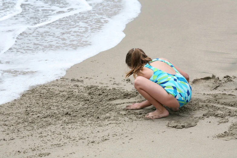 a woman kneeling down in the sand at the beach