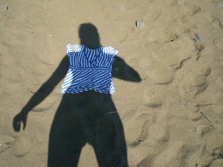 shadow on sandy beach of woman in striped shirt holding white frisbee