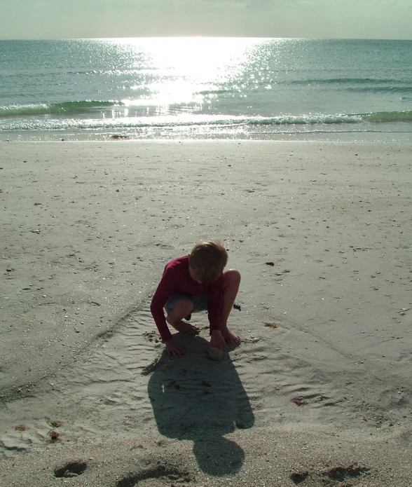  playing in sand at beach with the sun behind her