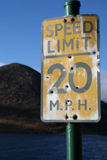 a speed limit sign with mountains and water in the background