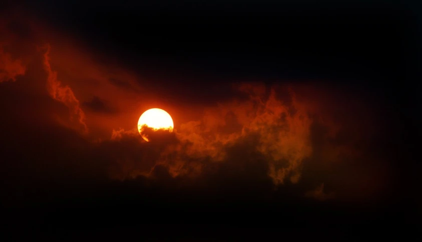 a bright sun peeking over the clouds behind it