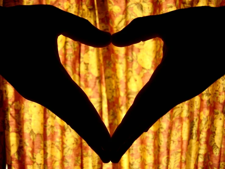 two hands making a heart shape with a curtain in the background