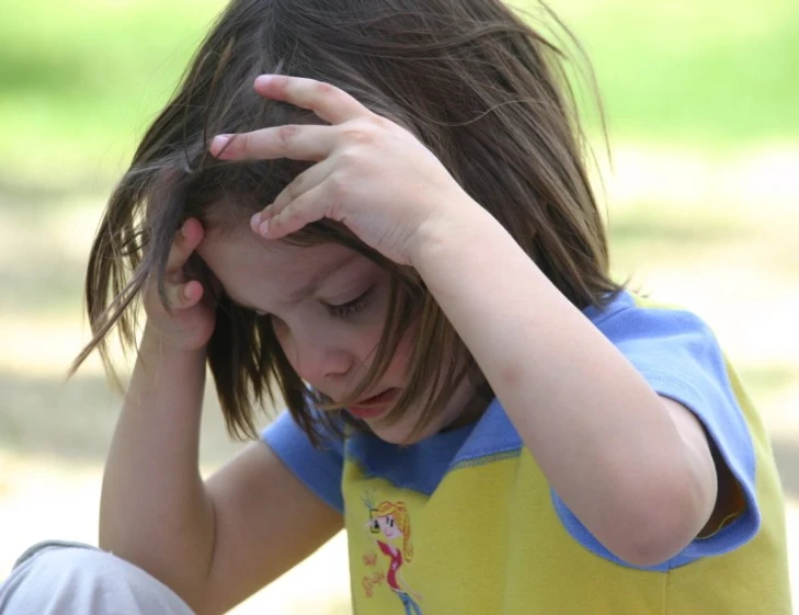 a little girl sitting in the park with her hand on her head