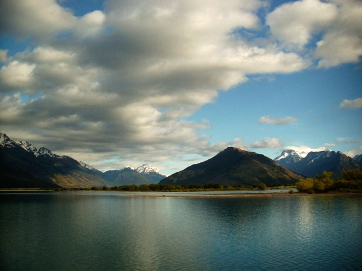 the mountains around a lake are seen against the cloudy sky