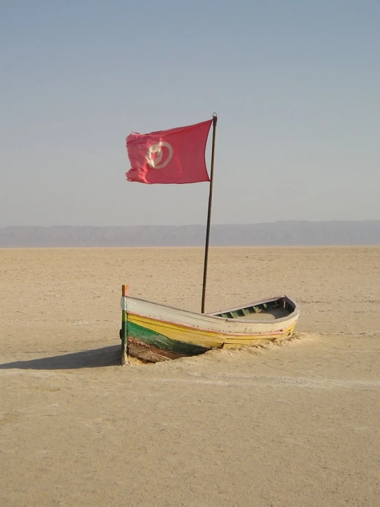boat with flag on sandy area in desert with blue sky