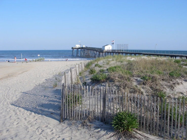 a wooden fence is next to the beach with buildings on it