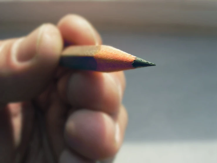 a person holding a rainbow colored pointed pencil