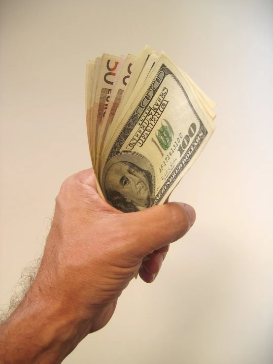 a man's hand holding up a five - dollar bill