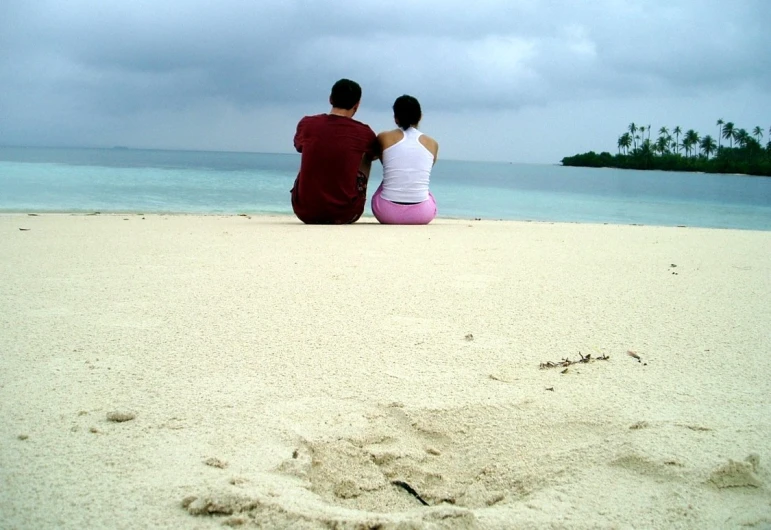 two people sitting on the beach watching the sea