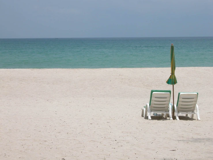 two chairs and an umbrella on a beach with the ocean in the background