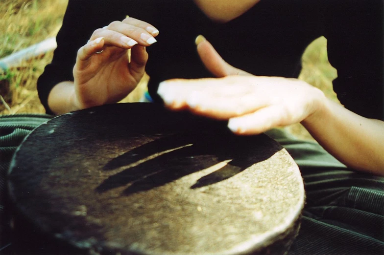 a woman in a black shirt is sitting by a wooden table and has her hands up with a musical instrument near by