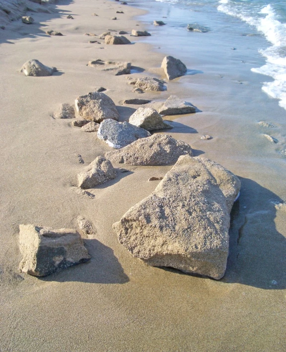 some rocks are on the sand by the water