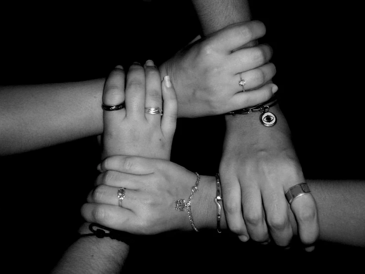 five hands stacked together showing many rings on their fingers