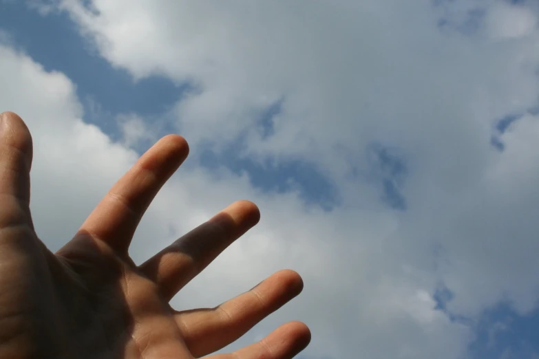 a hand is reaching up towards a sky with clouds
