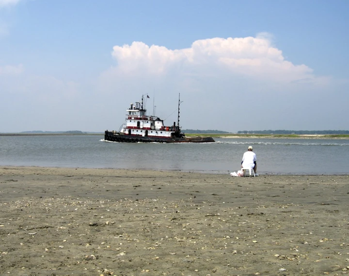 two people on beach watching a large boat in the water