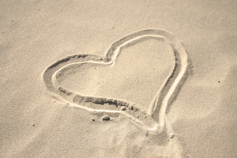 a heart drawn in the sand with a wave coming out