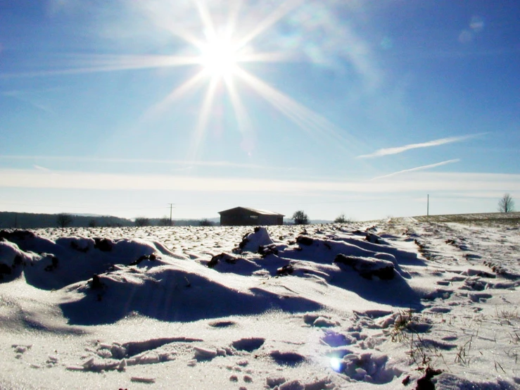 a snowy field covered in snow and a house under a bright blue sky