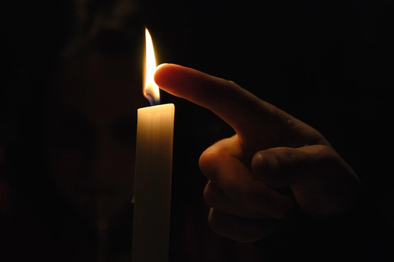a hand points at a lit candle with a flame