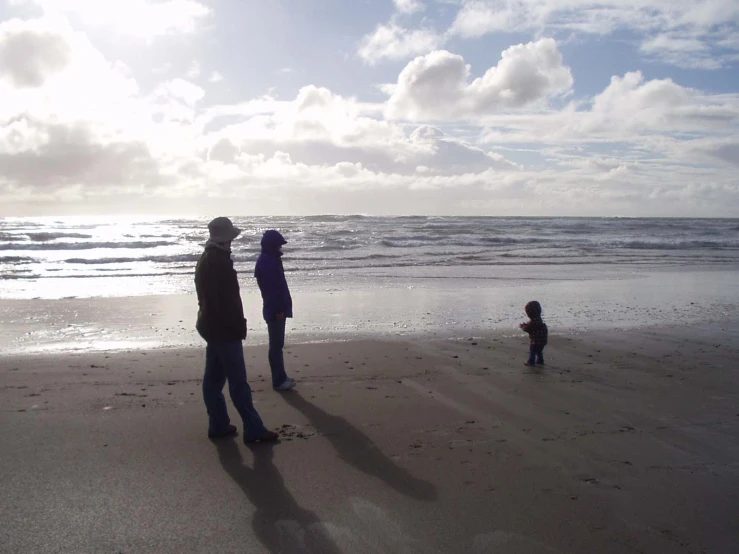 a group of people stand on the beach next to the ocean