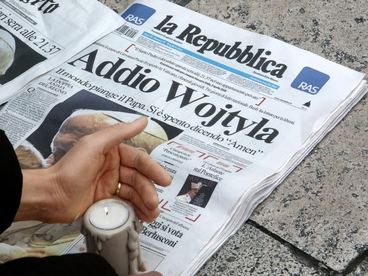 a person with a candle pointing to a newspaper with a political advertit