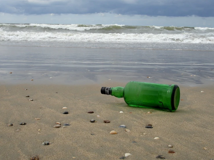 a green bottle lies in the sand on a beach