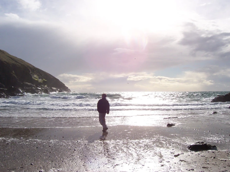 a person standing on the edge of a beach while looking at the water