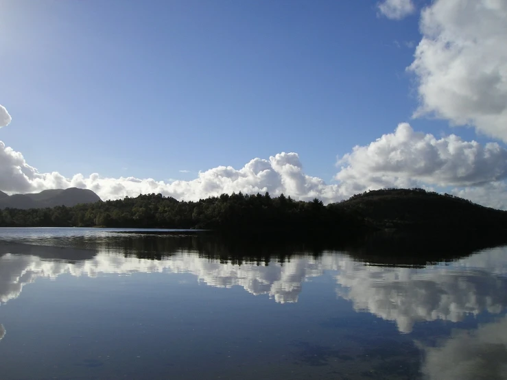 the water in the middle of a lake with clouds and a large island