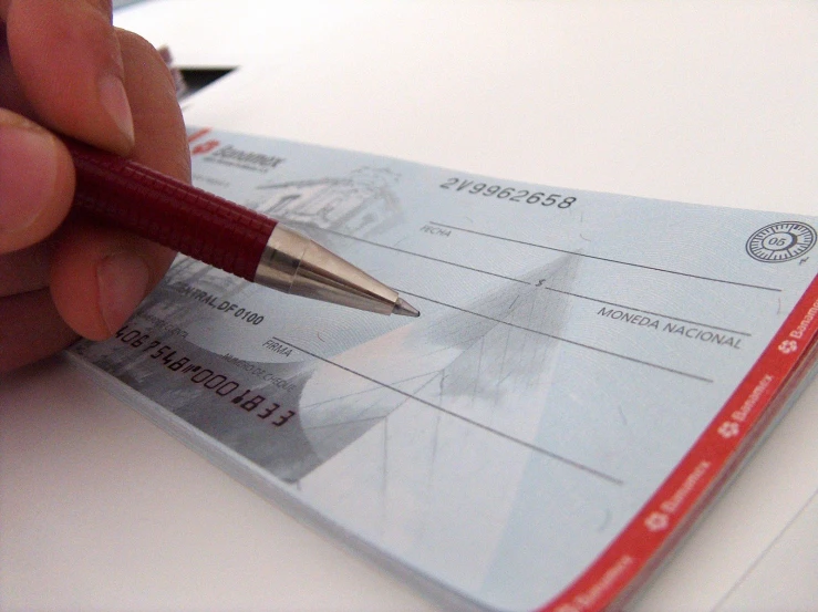 a person's hand holding a pen, writing on the cheque