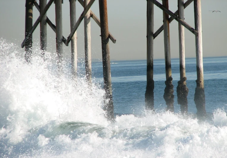 a pier with surf and birds flying around it