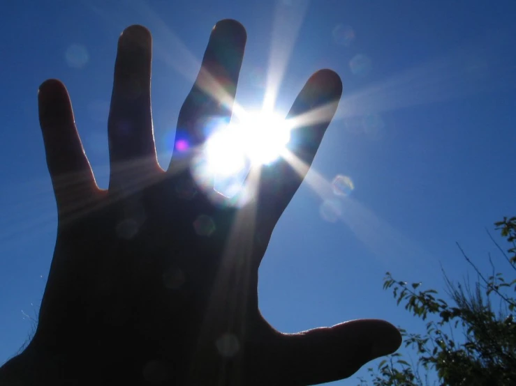 a person's hand with the sun coming down