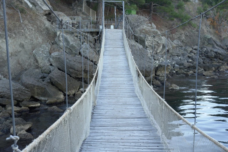 a hanging bridge stretching into the water near the rocky shoreline