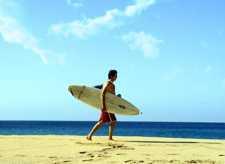 a young man is carrying a surfboard in the sand