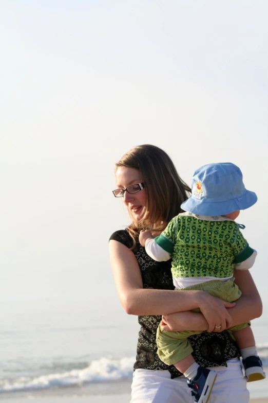 a woman holding a baby wearing sun glasses on the beach