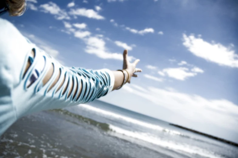 a woman who is standing near the ocean and reaching her hand to catch some air