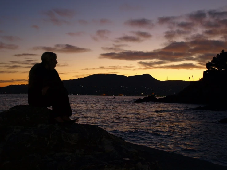 a man sitting on top of a rock next to a lake