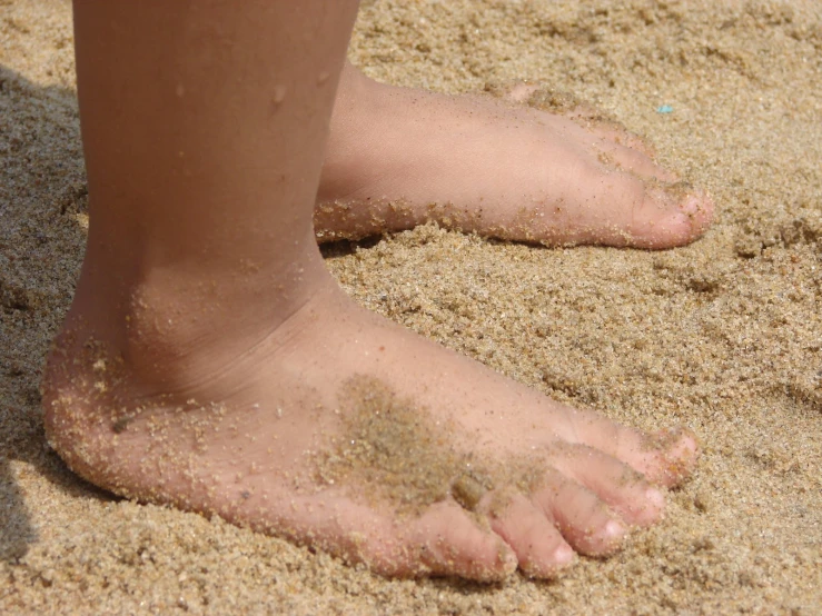 a child's bare feet sitting in the sand
