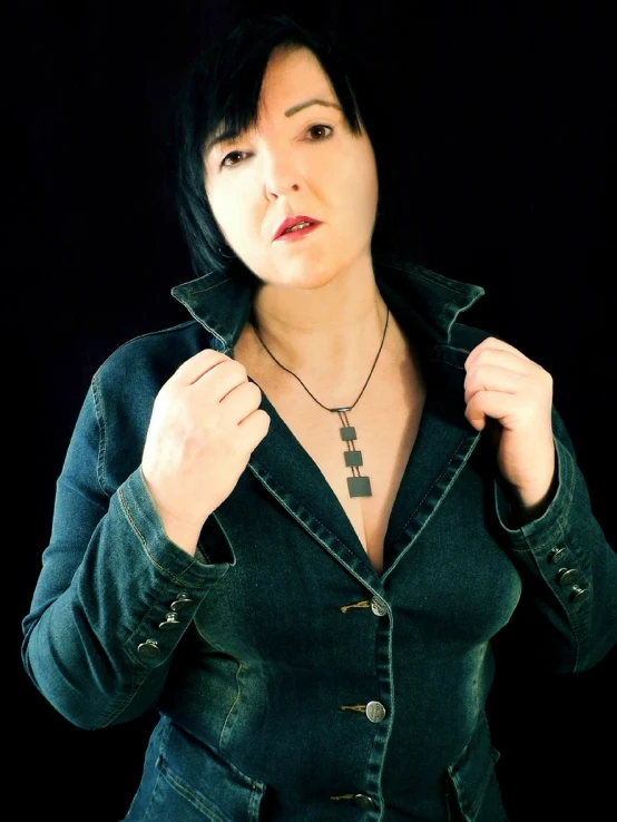 a woman wearing a jean jacket and holding a cross necklace