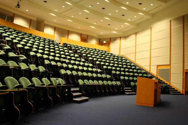 a lecture hall with green seats and an electronic podium