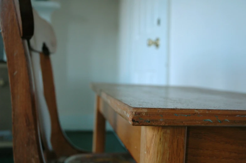 the back side of a wooden table with a wooden chair and door in the background