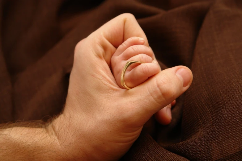 a man's hands are holding a tiny gold ring